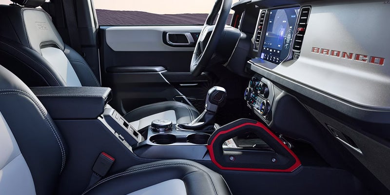 Interior of a new Ford Bronco, with black and white leather seats, shifter, touchscreen, and red "BRONCO" logo.