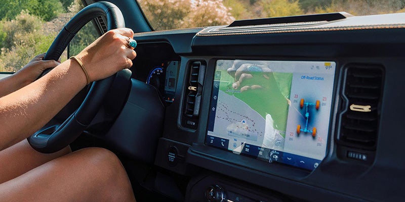 Hands on a steering wheel, with a large in-car display showing a map and "Off-Road Status."