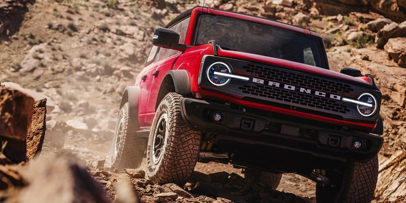 A red Ford Bronco off-road SUV climbing over rocky terrain in a desert-like landscape.