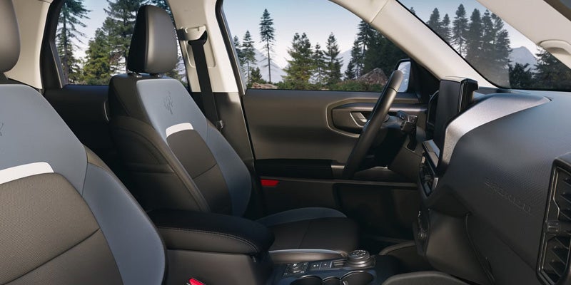 The interior of a vehicle with two-tone grey and black seats, a visible steering wheel, and a forested mountain background.