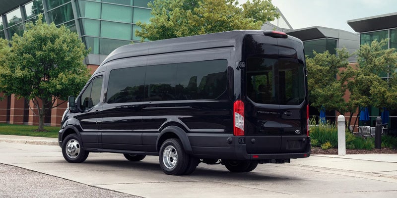 Rear passenger side view of a black Ford Transit van with tinted windows parked on concrete.