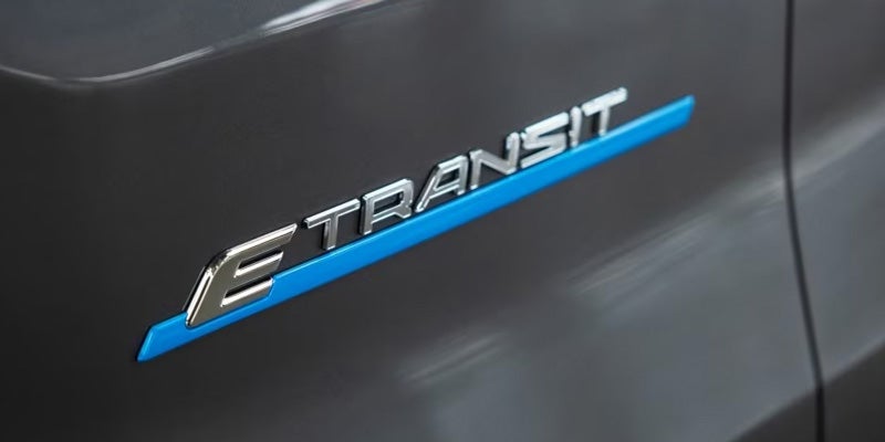 Chrome "E-TRANSIT" emblem with a blue underscore on a dark gray vehicle body.