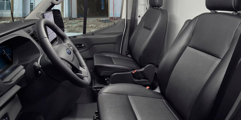 Interior of a black van cabin with the driver's seat, steering wheel, infotainment system, and two passenger seats.