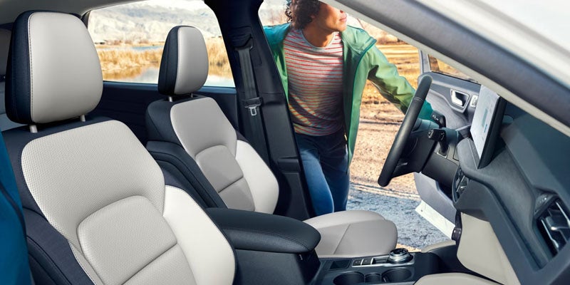 Interior view of a car with two-tone blue and cream seats. A person stands outside the open driver's door.