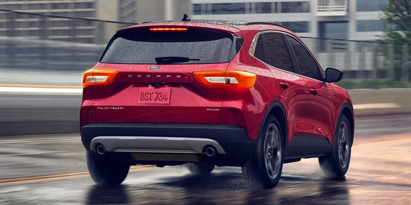 Rear view of a red Ford Escape Platinum SUV driving on a wet road with blurred background.