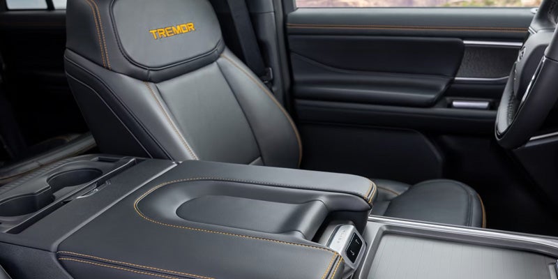 Interior of a truck cabin showing a black leather seat with "TREMOR" in orange, orange stitching, and center console.