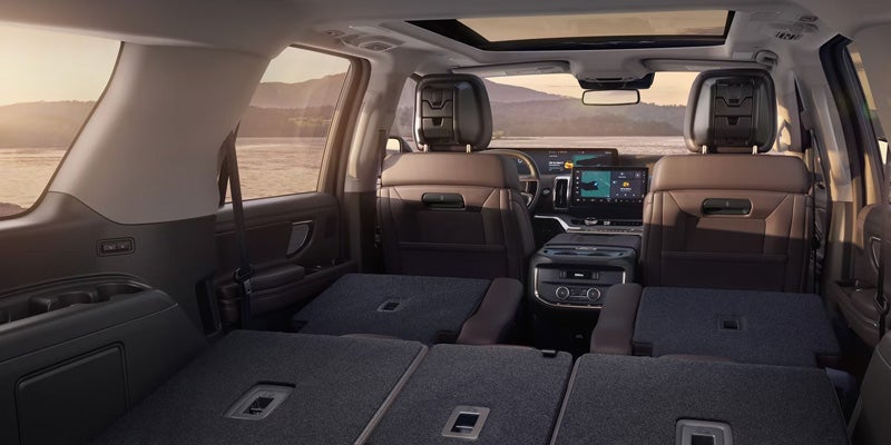 Interior of a brown SUV showing all rear seats folded flat, creating a large cargo area, with a sunset over water in the background.
