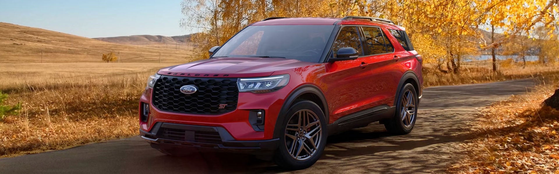 A red Ford Explorer SUV parked on a paved road surrounded by golden autumn trees and dry, grassy hills.