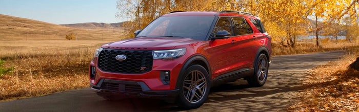 A red Ford Explorer SUV parked on a paved road surrounded by golden autumn trees and dry, grassy hills.