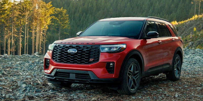 Red Ford Explorer ST SUV parked on a rocky, uneven clearing with pine trees in the background.