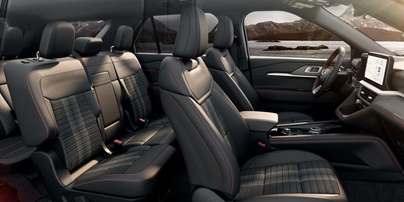 Spacious gray car interior with red stitching, plaid seat inserts, and a widescreen display, with mountains out the window.