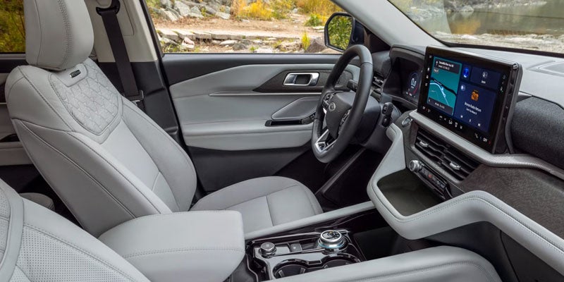 Interior of a modern car from the passenger seat, showing light grey leather seats, dashboard, and large touchscreen.