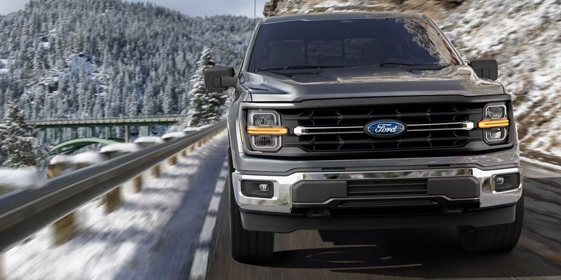 Front view of a dark gray Ford F-150 pickup truck on a winding snowy mountain road.