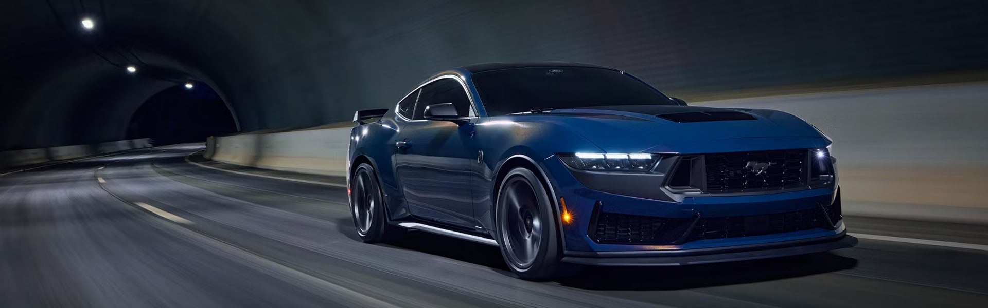 Dark blue performance car speeding through a tunnel, head-on.