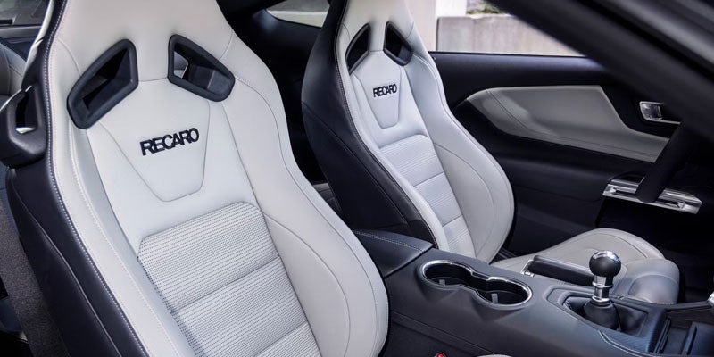 Two white and black Recaro sports seats with branding, a center console, and a black shifter knob in a car interior.