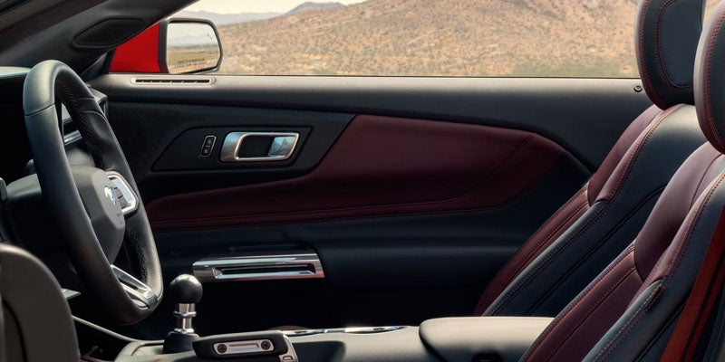 Red and black interior of a car, showing the steering wheel, gear stick, door, and passenger seat.