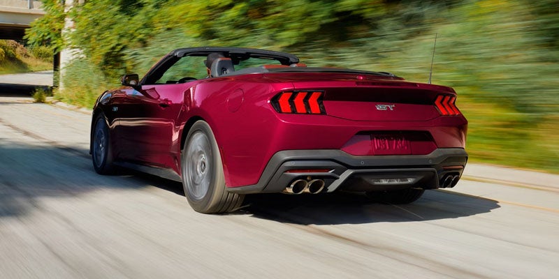 Rear view of a new red Ford Mustang GT convertible speeding on a sunlit road.