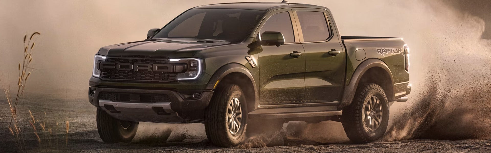 A dark green Ford Ranger Raptor pickup truck kicking up dust on a sandy off-road track.