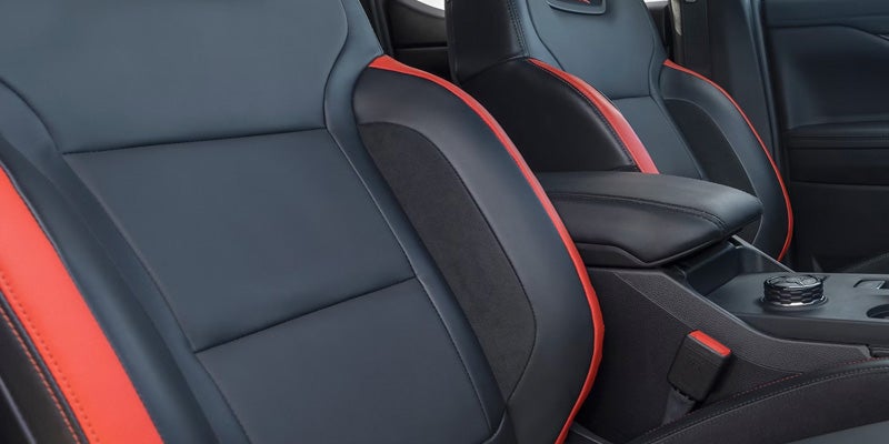 Black leather sports seats with red trim and an armrest in a car interior.