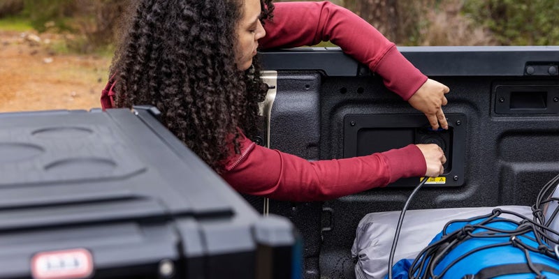 A woman with curly hair in a maroon top plugging a blue cord into an outlet in the bed of a truck.