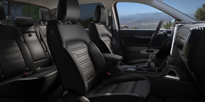 Black leather car interior with textured seats and a steering wheel, view of mountains outside the window.