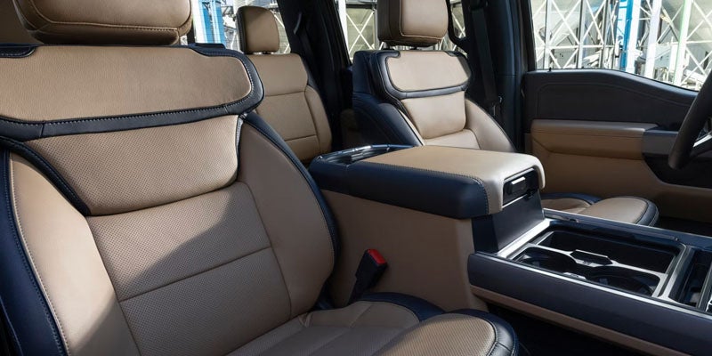 Interior of a vehicle featuring tan and dark blue leather seats, armrest, and console.