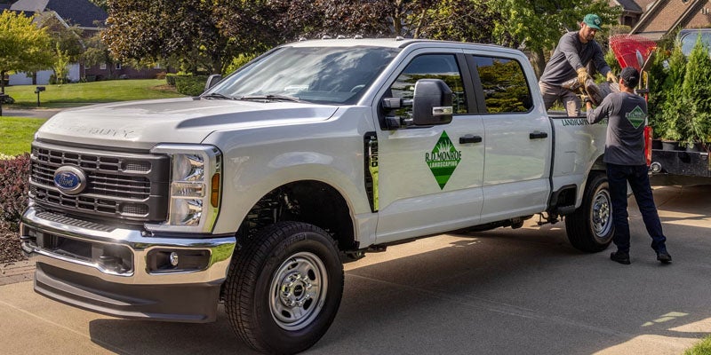 Two men unload equipment from a white Ford F-250 Super Duty pickup truck with a "R.D. Monroe Landscaping" logo.