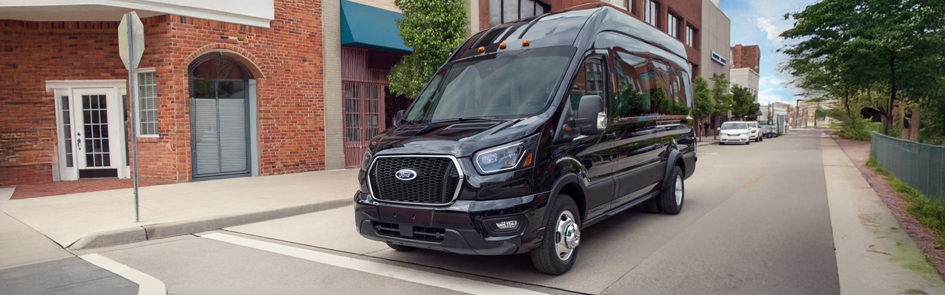 Black Ford Transit passenger van parked at an angle on a city street in front of brick buildings.