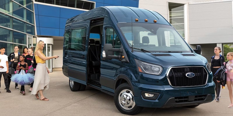 Woman with remote opening the side door of a dark teal Ford passenger van as children gather around it.