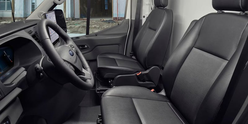 Interior of a black van, showing the driver's seat, passenger seat, steering wheel, and a large tablet screen.
